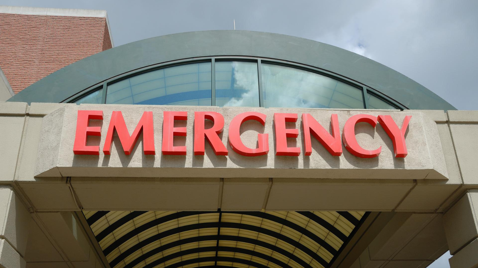 Front eines Krankenhauses, über dem breiten Eingang steht in großen roten Buchstaben das Wort EMERGENCY
