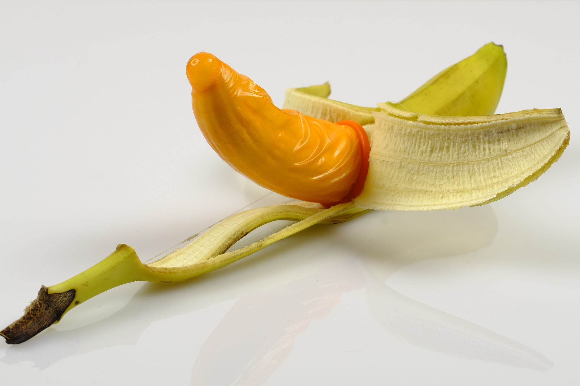 oranges Kondom, über die Frucht einer halb geschälten Banane gezogen